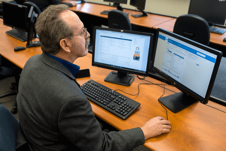 Financial Services student wearing a suit and sitting and analyzing stocks on a computer