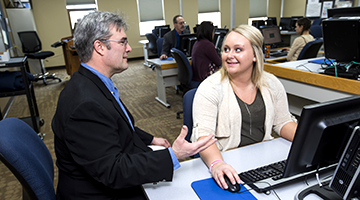 An instructor explaining a finance concept to a student sitting at a computer