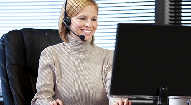 An office support specialist wearing a headset and looking at a computer