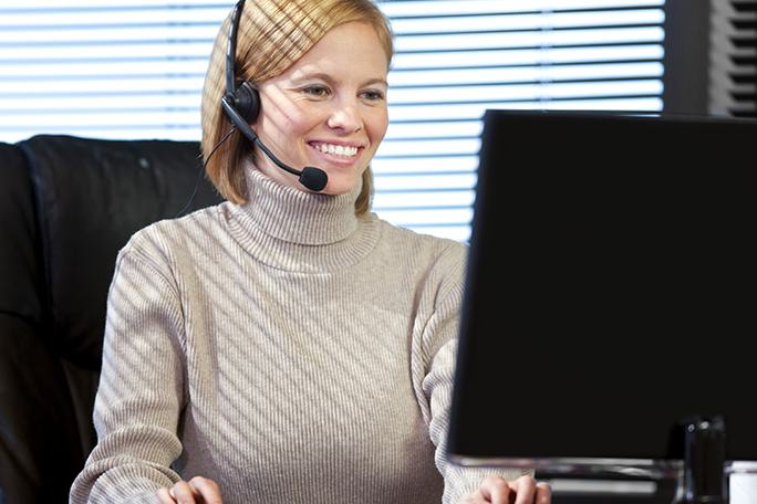 A business professional talking on a headset while looking at computer