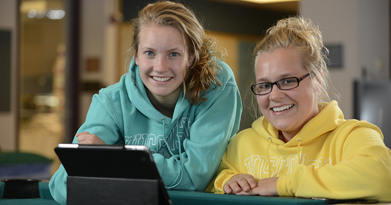 Two students work on tablet leaning on a pool table